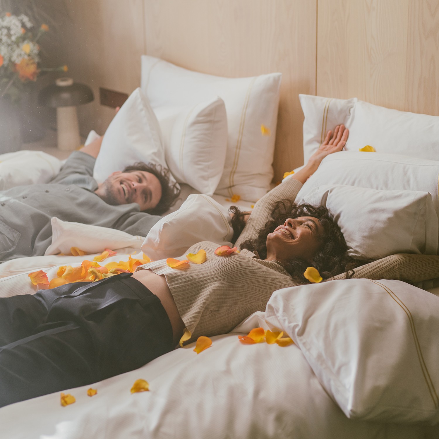 Hotel Reiters Supreme - Frau und Mann lassen sich ins Bett fallen mit orangen Rosenblüten